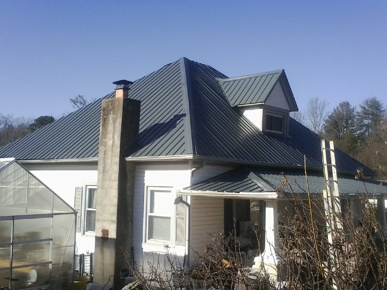 Dark blue standing seam metal roof on a white farmhouse with dormer — Slate & Tile Roof Repair by Roofing Brothers in Swain