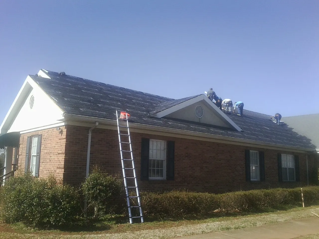 Crew tearing shingles off a brick ranch roof with a ladder set — Emergency Roof Repair work by our crew in Swain