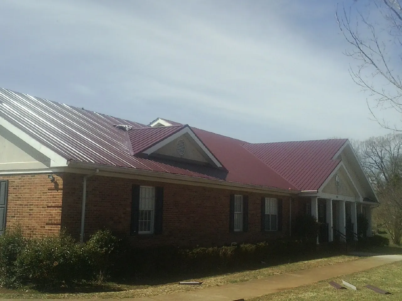Red metal roof with gabled entries on a long brick building, from a Hail Damage Roof Repair job in Swain