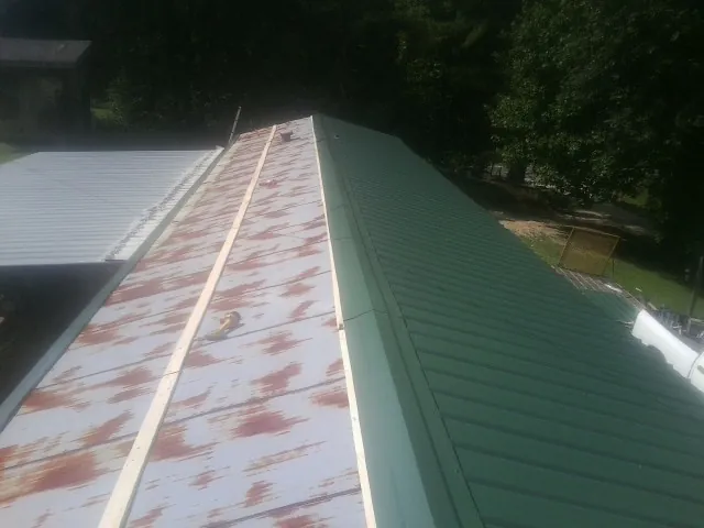 Old rusted panels beside newly installed green metal roofing — Wind Damage Roof Repair by Roofing Brothers in Swain