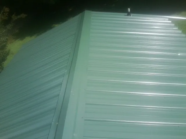 New green metal panels meeting at the ridge of a roof — Flat Roof Repair work by our crew in Swain