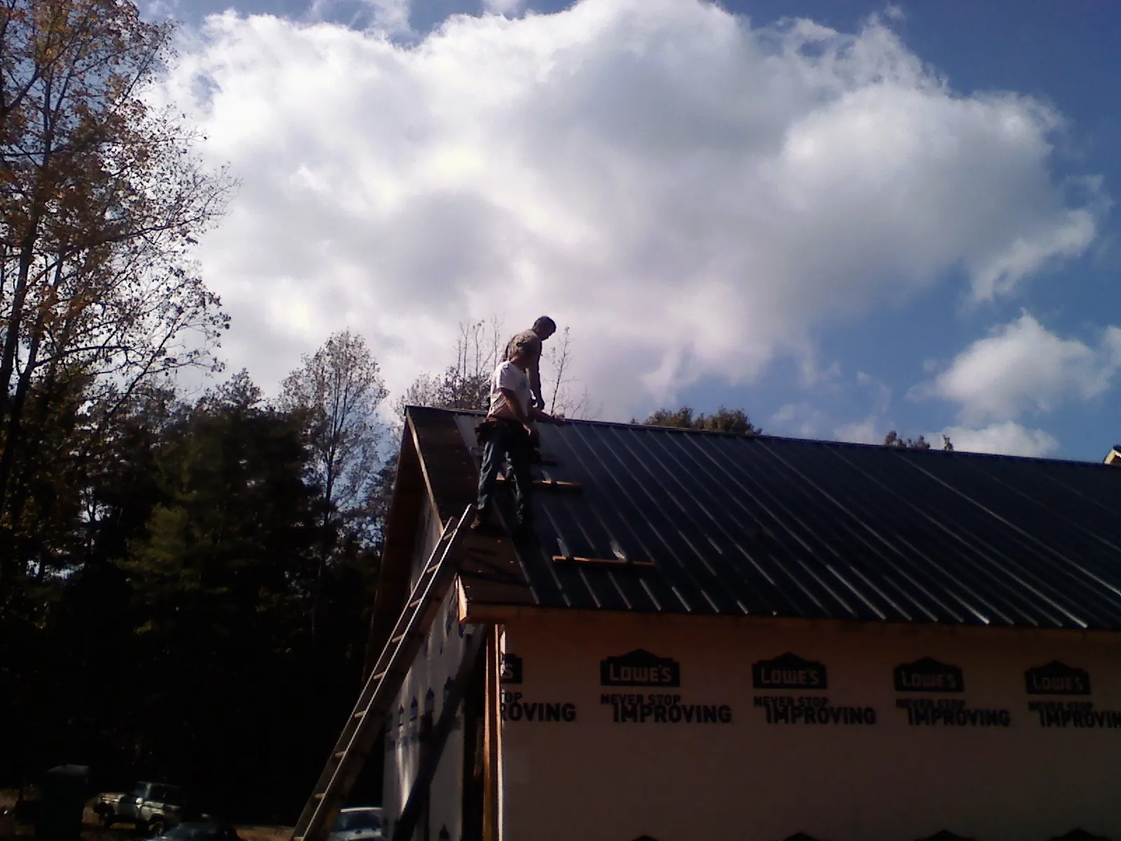 Roofer fastening dark metal panels high against a cloudy sky, from a Roof Inspection job in Swain