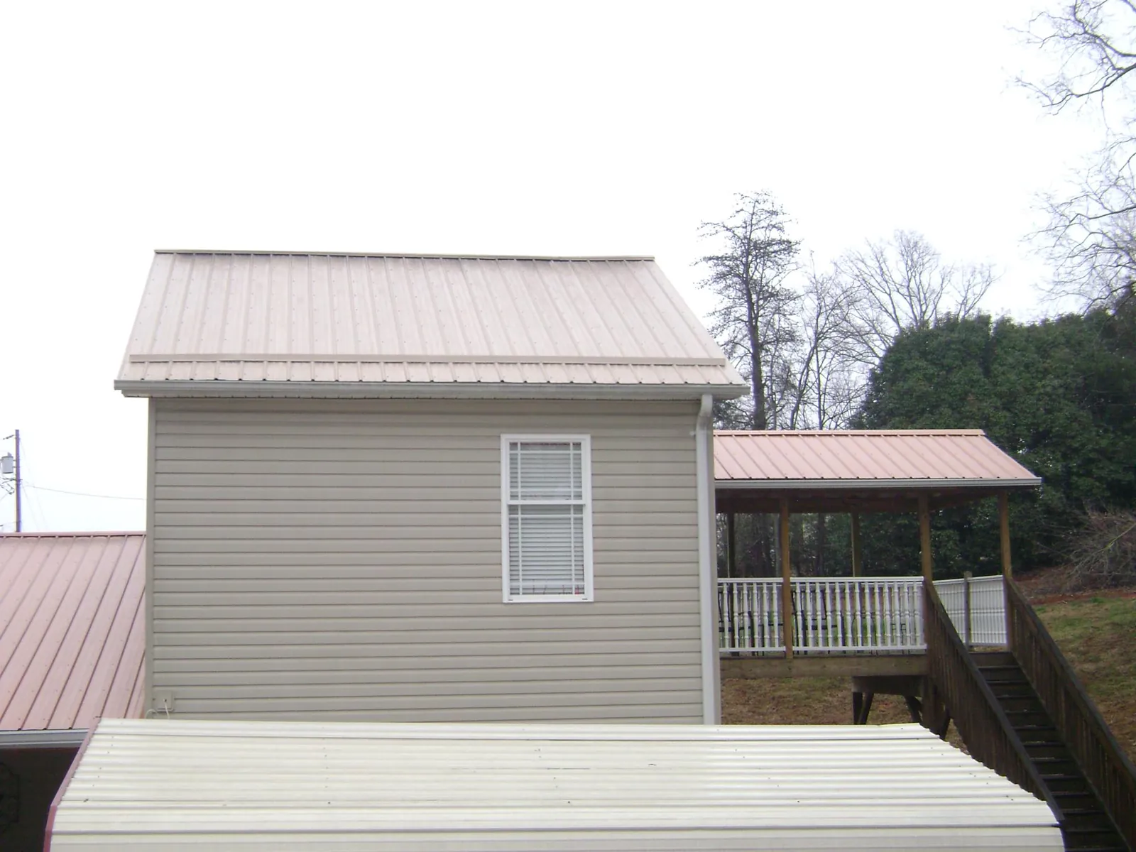 Tan metal roofs on a two story addition and attached porch, from a Roof Replacement job in Swain