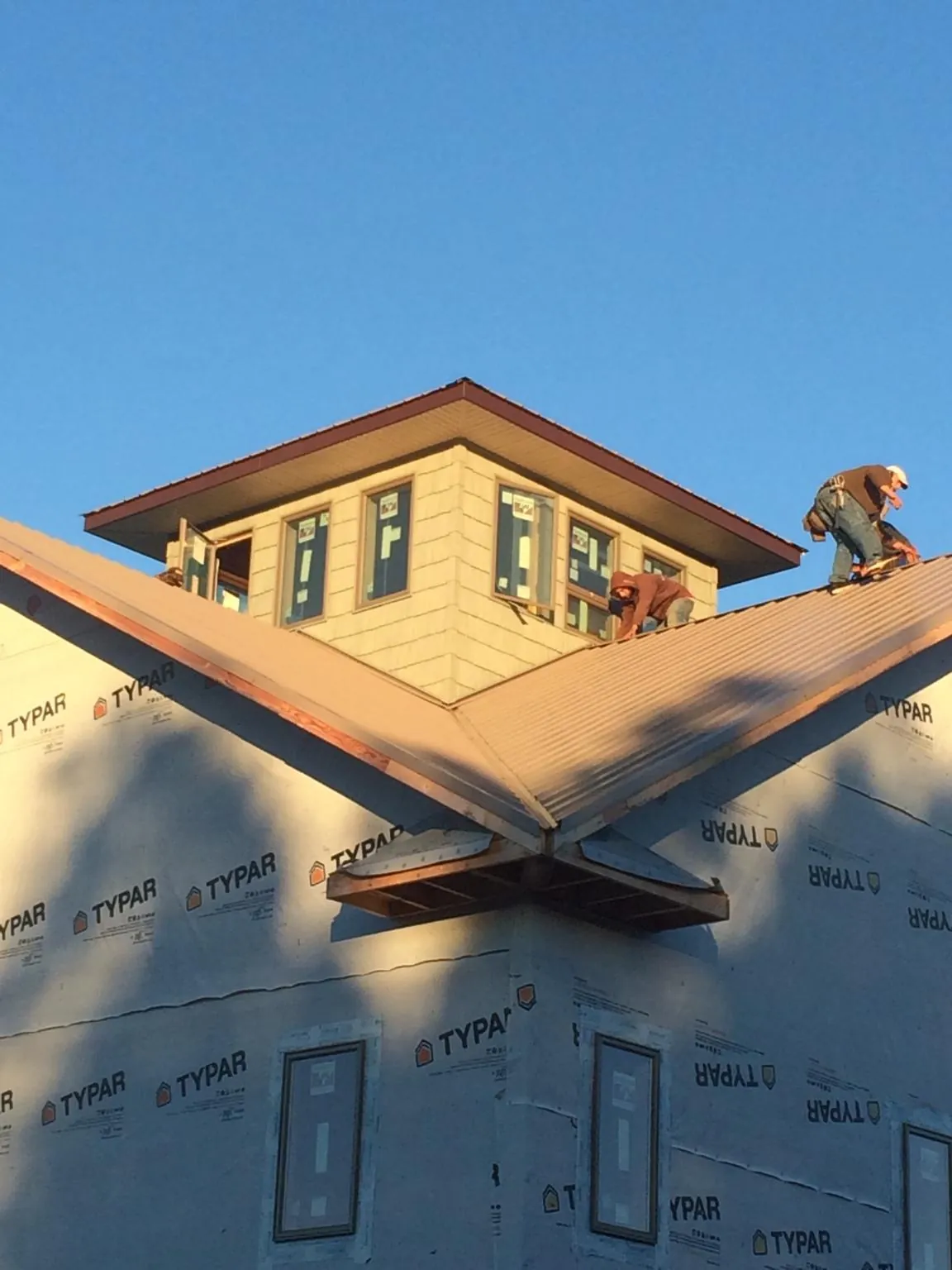 Roofers working around a rooftop cupola on a new metal roof at sunset — Roof Waterproofing in Swain by Roofing Brothers